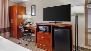 Una habitación de hotel con una cama, un escritorio con una computadora, un microondas, un refrigerador, un televisor y una lámpara.