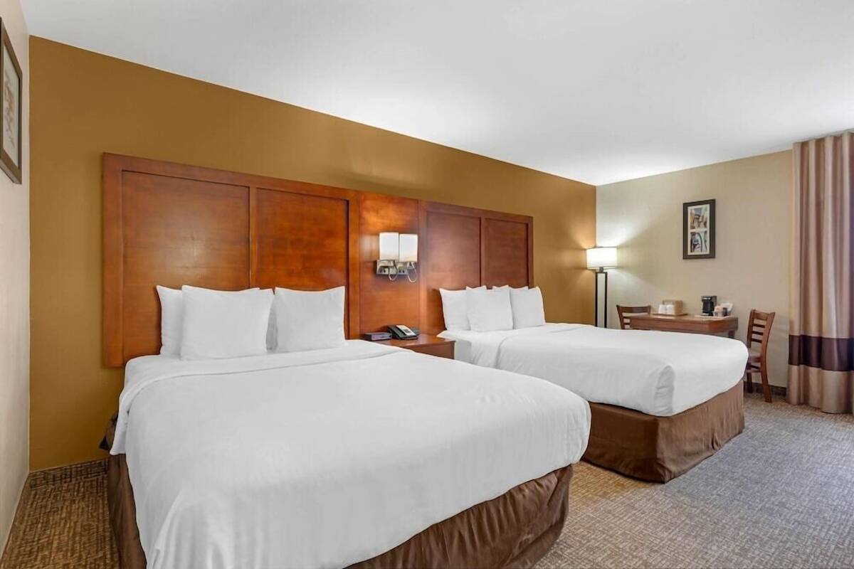 A hotel room with two beds, a desk, a chair, a lamp, and a framed picture on the wall.