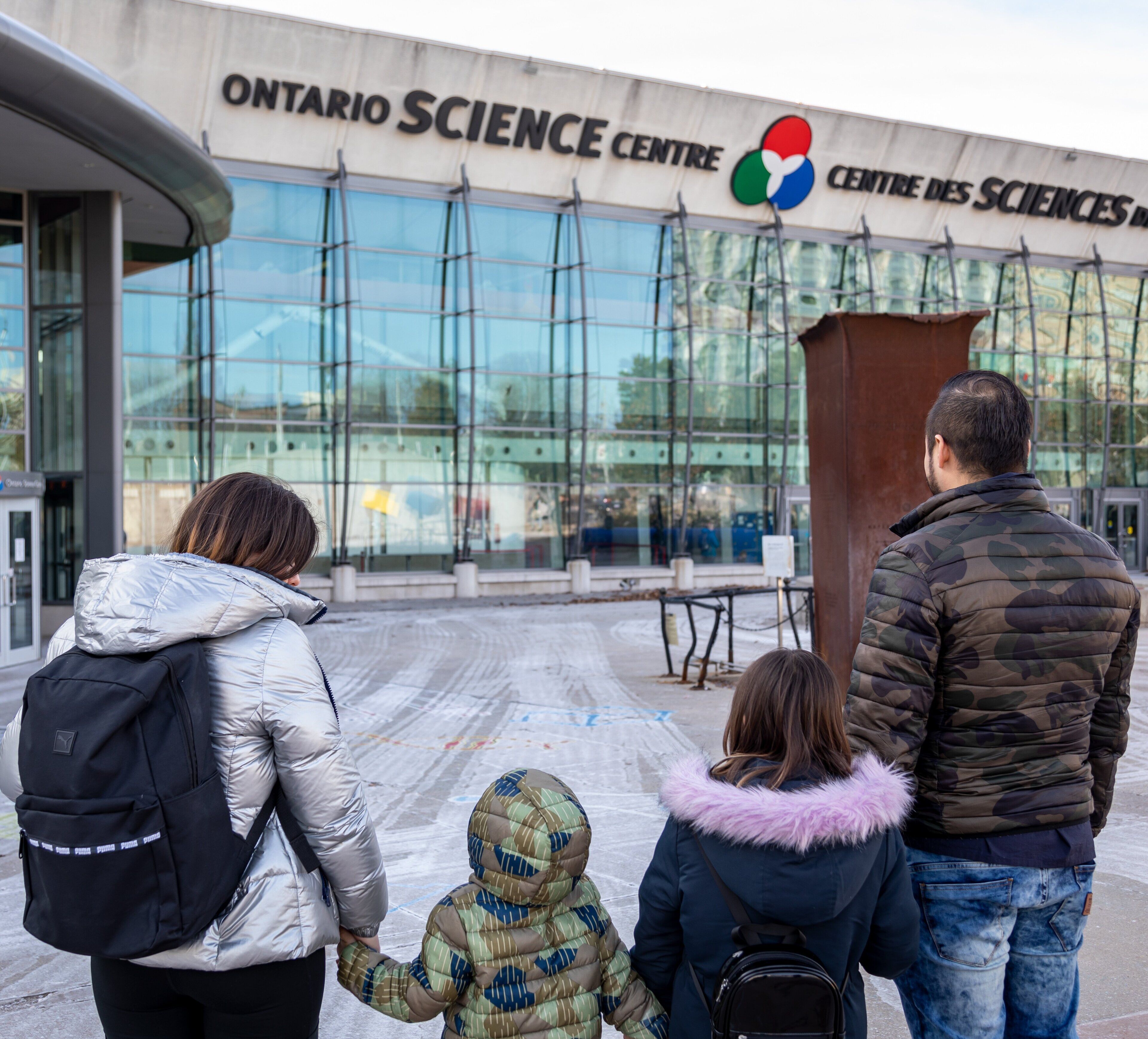 En familie foran Ontario Science Centre, der holder i hånd.