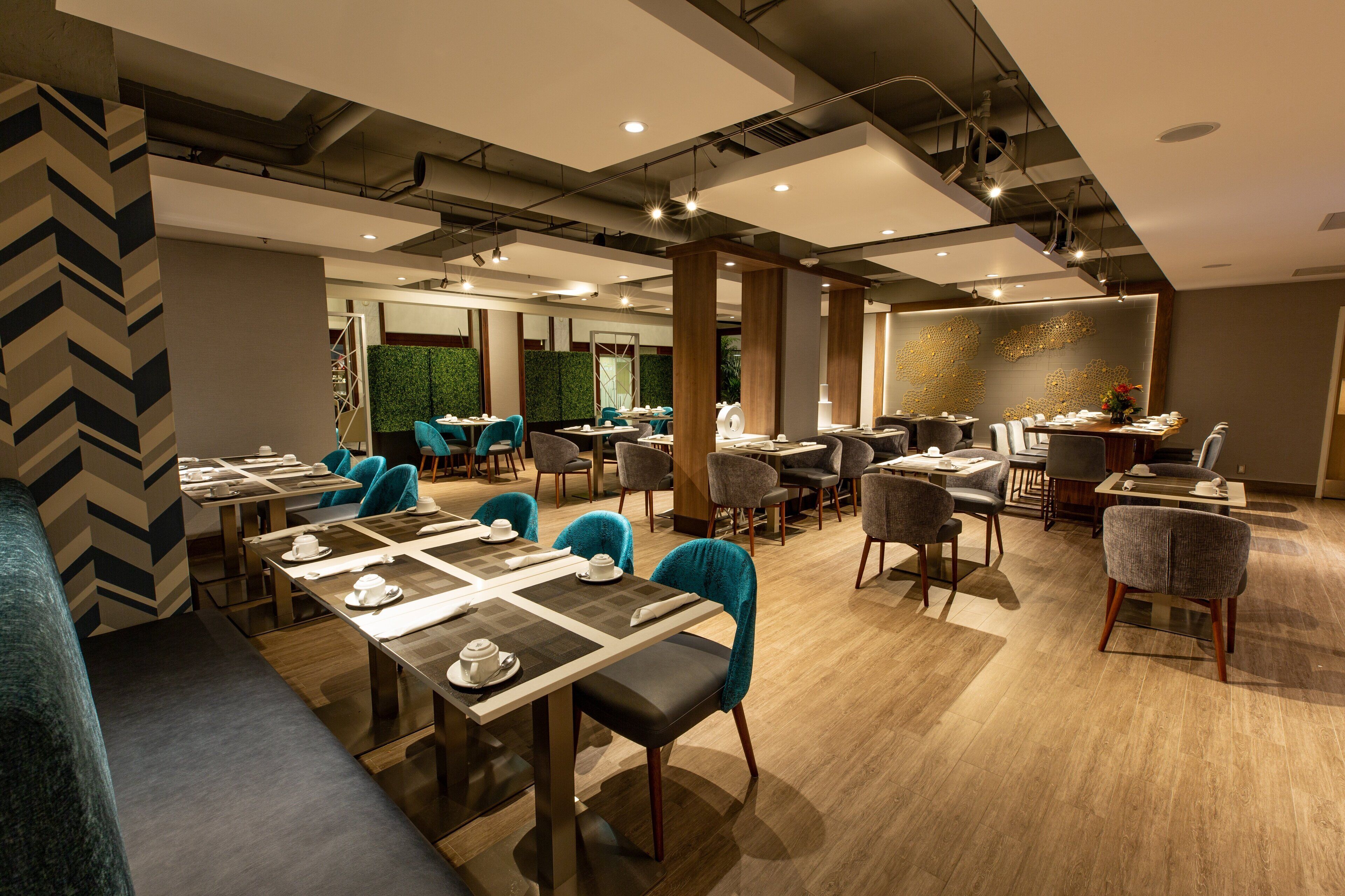 A modern dining area with multiple tables and chairs, a green wall, and a decorative wall piece.