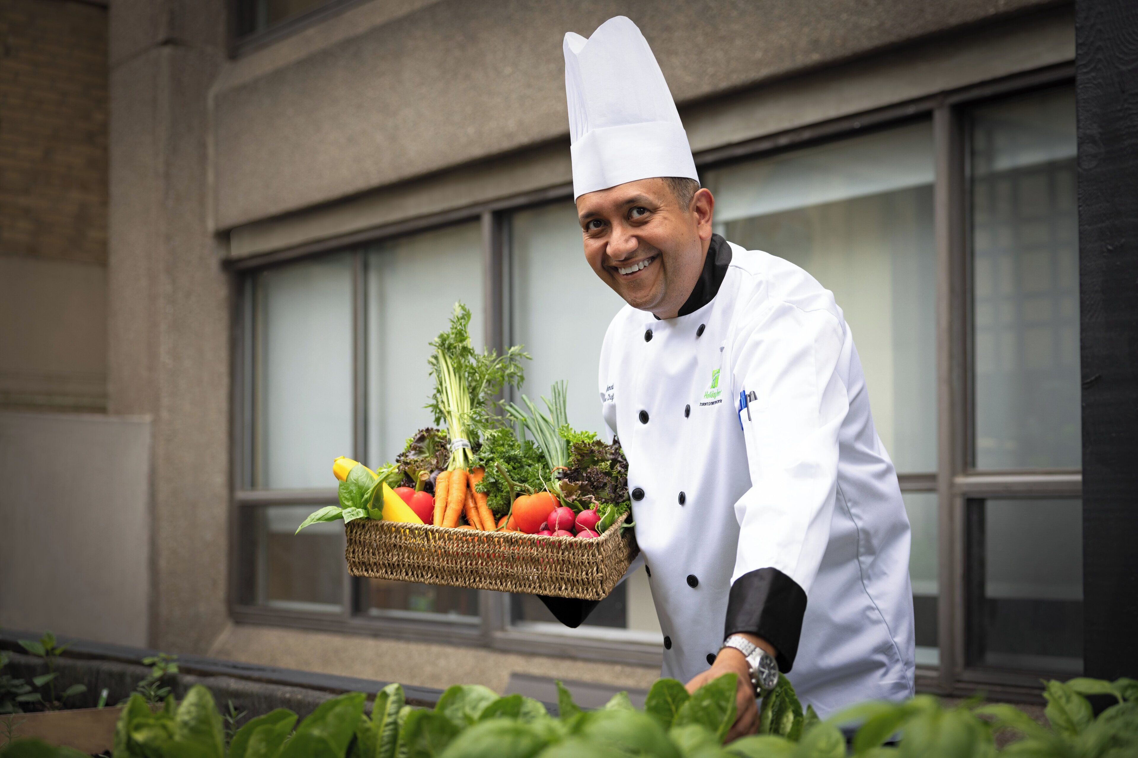 A chef holding a basket of fresh vegetables.
