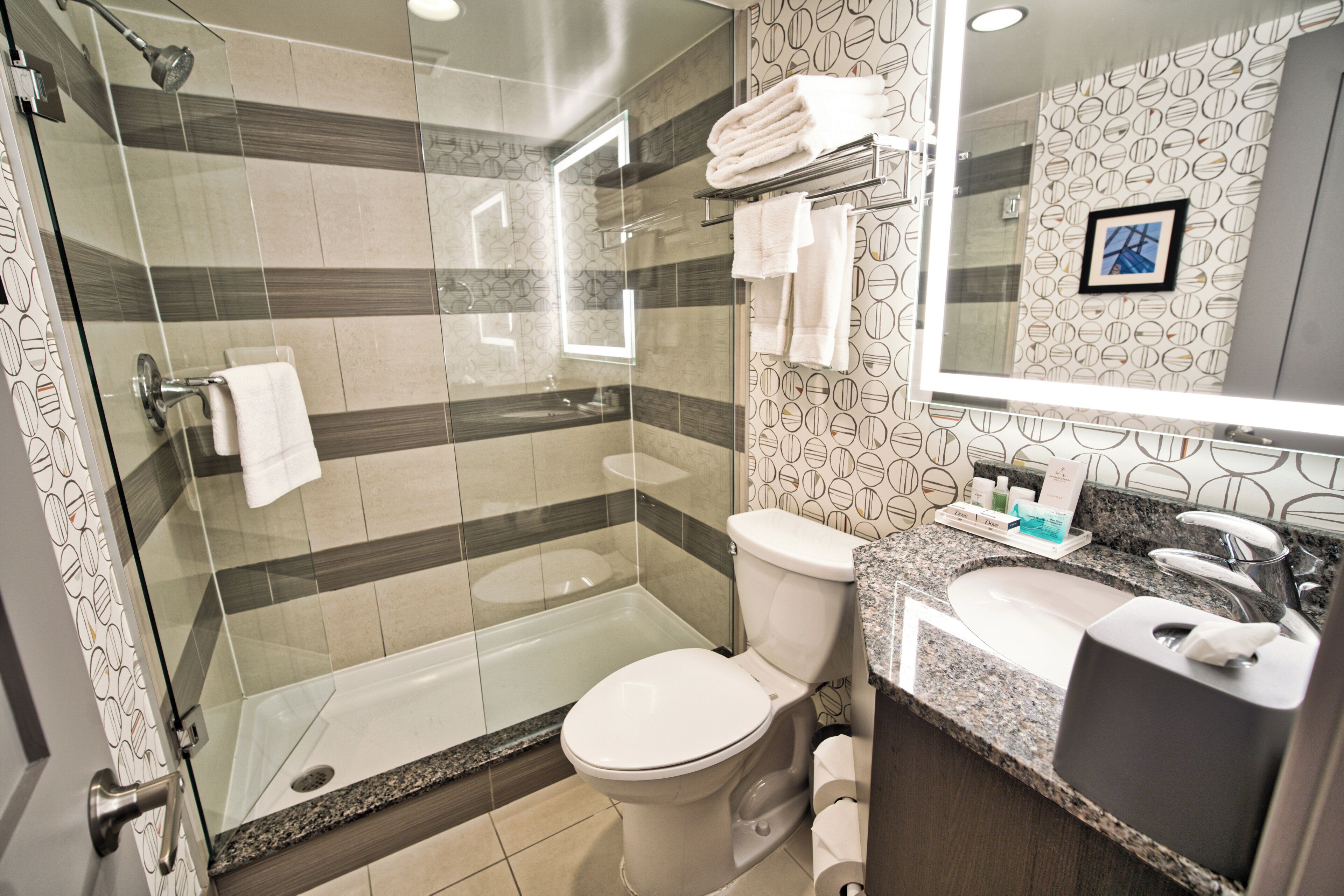 Een moderne badkamer met een glazen douchecabine, toilet en een wastafelmeubel met een wastafel en spiegel.
