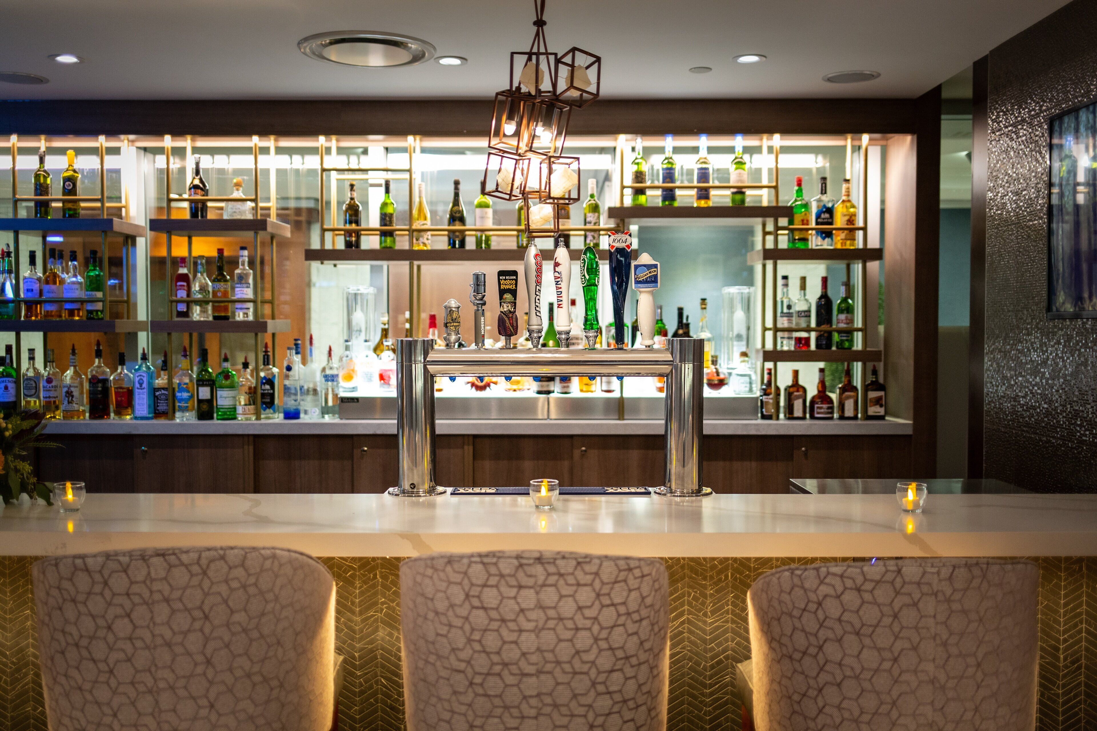 A bar area with a variety of liquor bottles, a bar counter, and seating with patterned chairs.