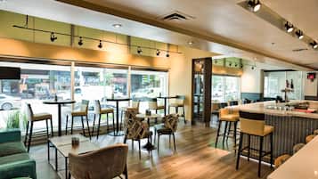A modern cafe with wooden flooring, comfortable seating, and large windows offering a view of the street.
