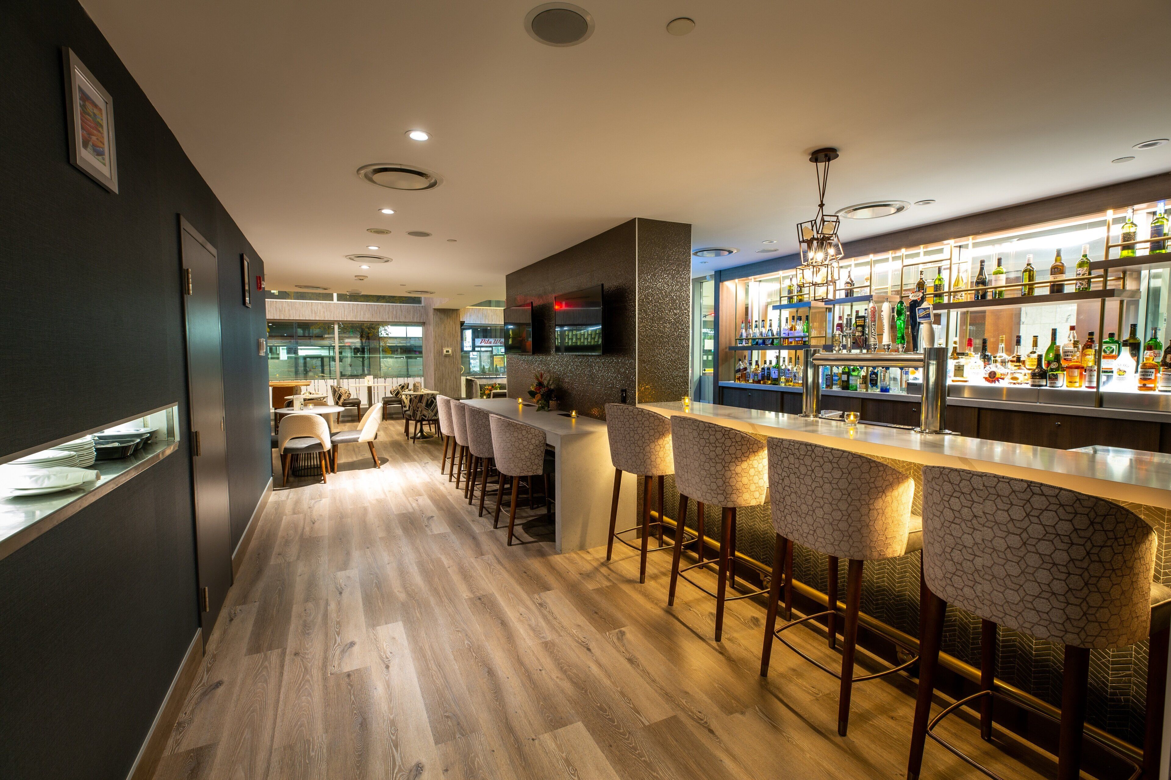 A modern bar area with a long counter, bar stools, and a well-stocked liquor display.