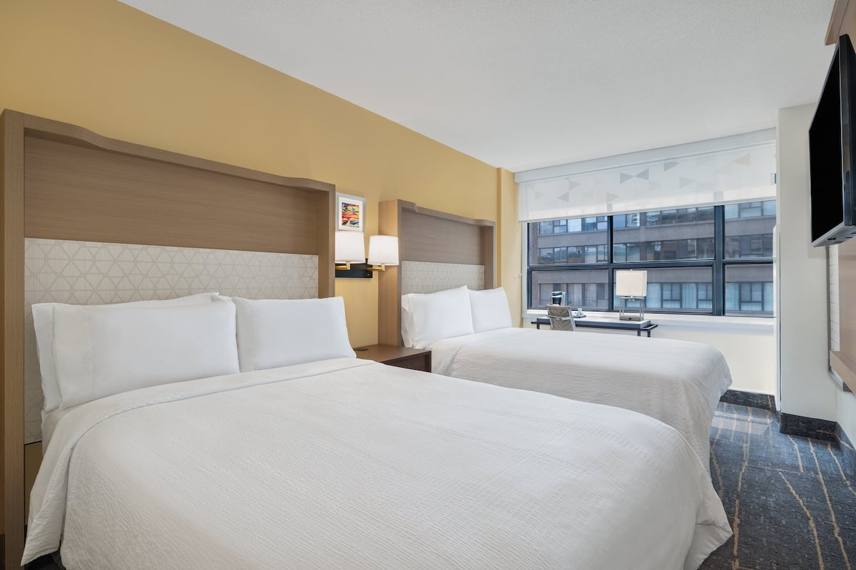 Hotellihuone, jossa on kaksi sänkyä, työpöytä, tuoli, televisio ja ikkuna, josta avautuu näkymä kaupunkiin.