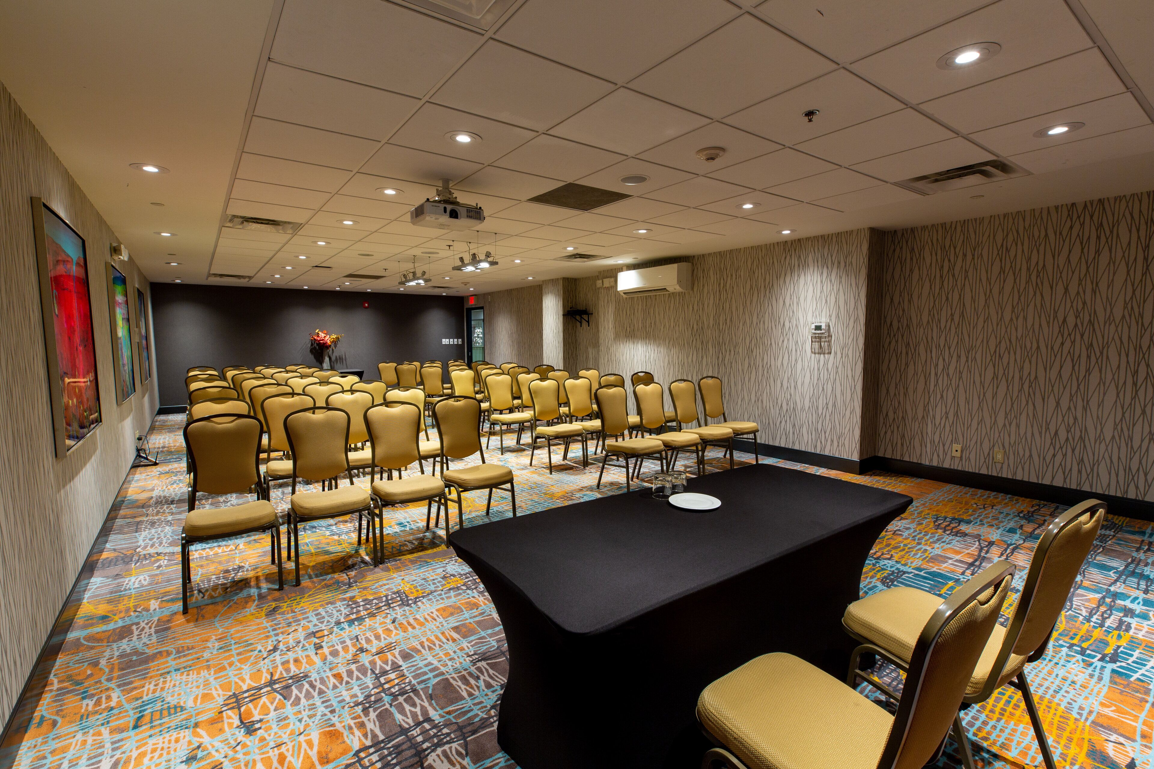 A conference room with rows of chairs, a long table, and a projector on the ceiling.