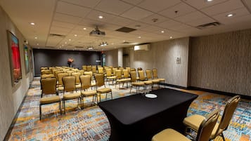 A conference room with rows of chairs, a long table, and a projector on the ceiling.