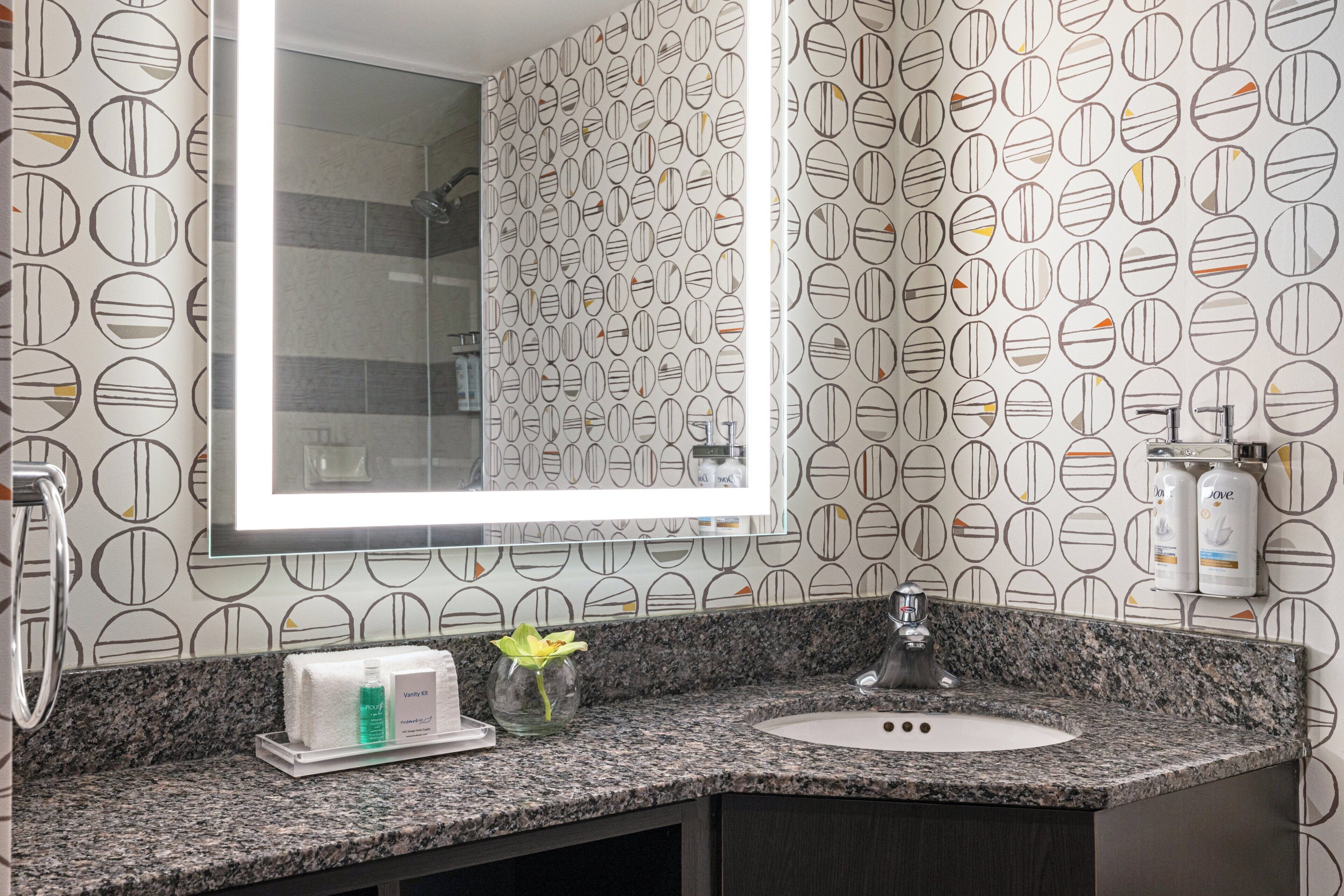 A bathroom with a granite countertop, a sink, a mirror, and a vanity area.