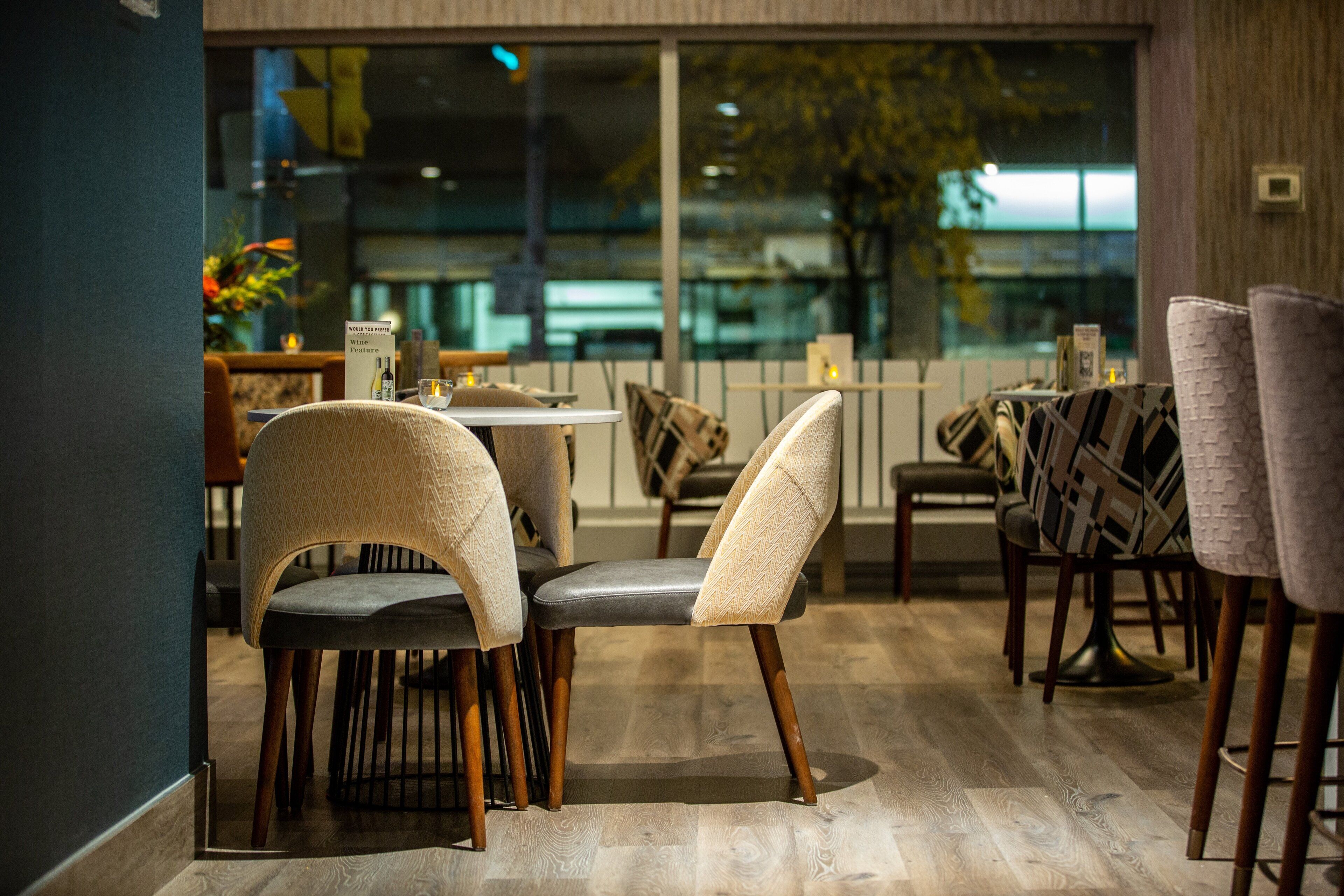 Un comedor moderno con suelo de madera, sillas tapizadas y un separador de vidrio.