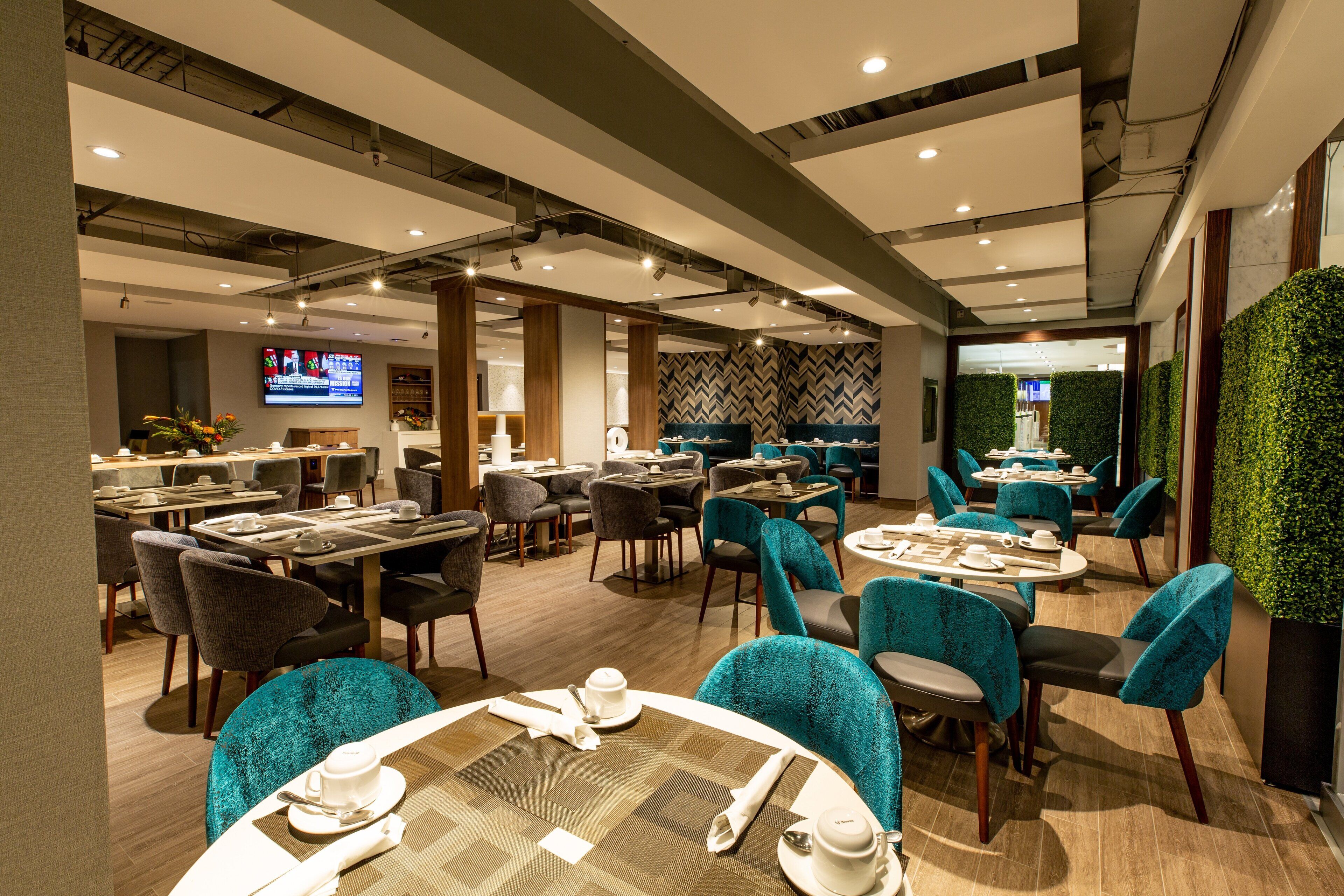 Een moderne eetruimte van een hotel met ronde tafels, teal stoelen en een grote flatscreen televisie op de achtergrond.