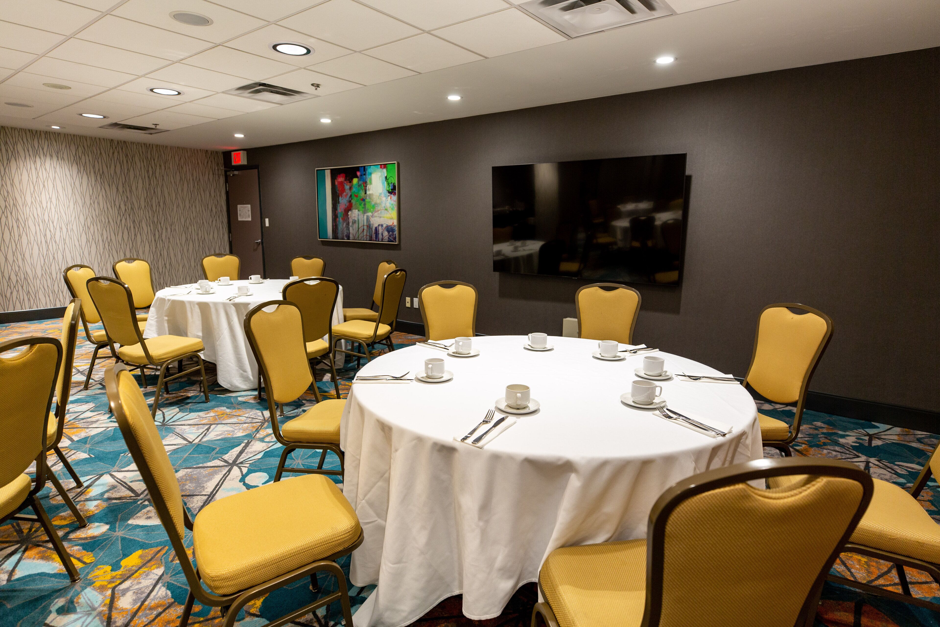 Une salle de conférence avec des tables rondes, des chaises jaunes et un tapis à motifs.