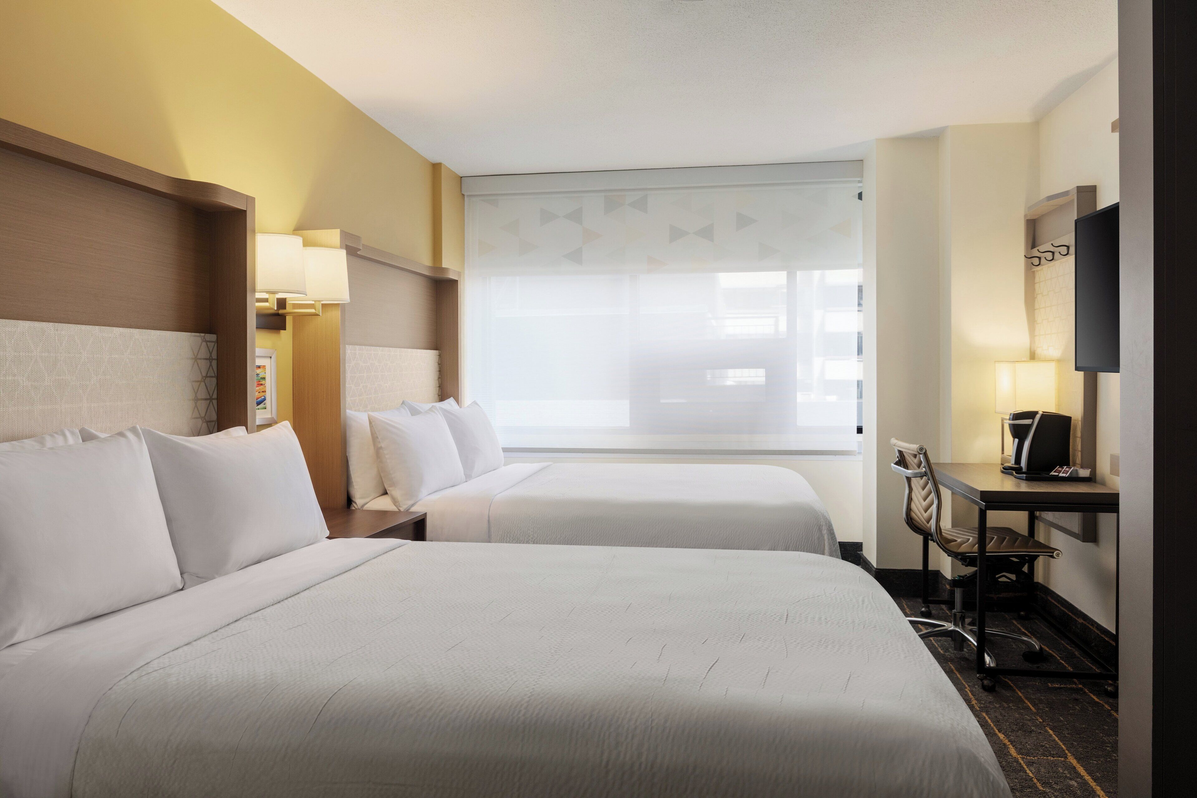 A hotel room with two beds, a desk with a chair, a TV, and a window with a view.