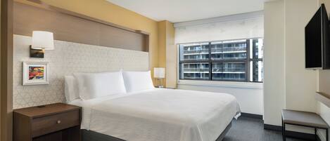 A hotel room with a large bed, bedside tables, a TV, and a window with a city view.