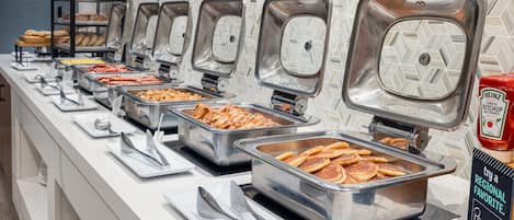 A buffet with various food options, including meats, cheeses, and pancakes.