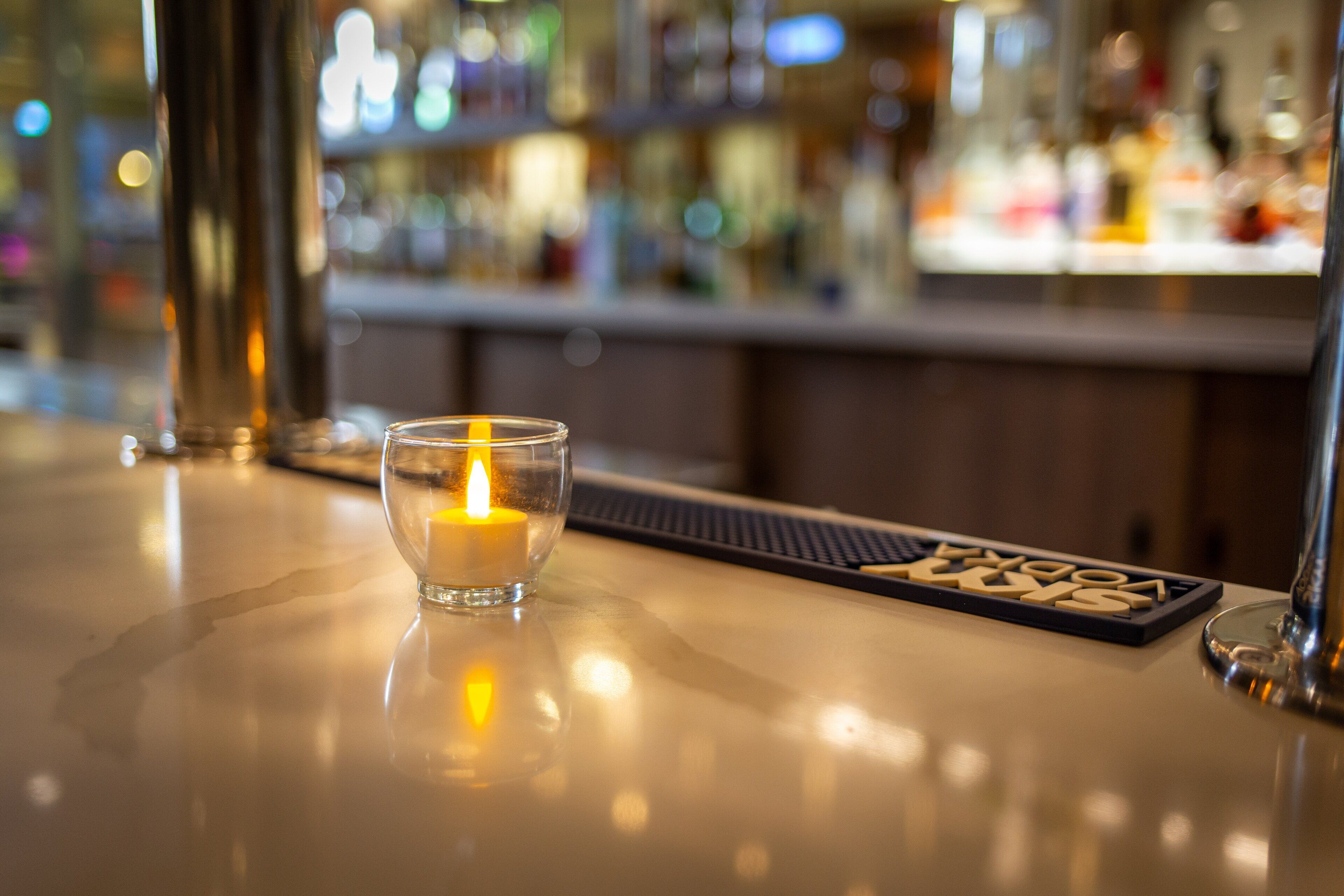 Een bar met een kaars op een reflecterend oppervlak, een barmat met de tekst 