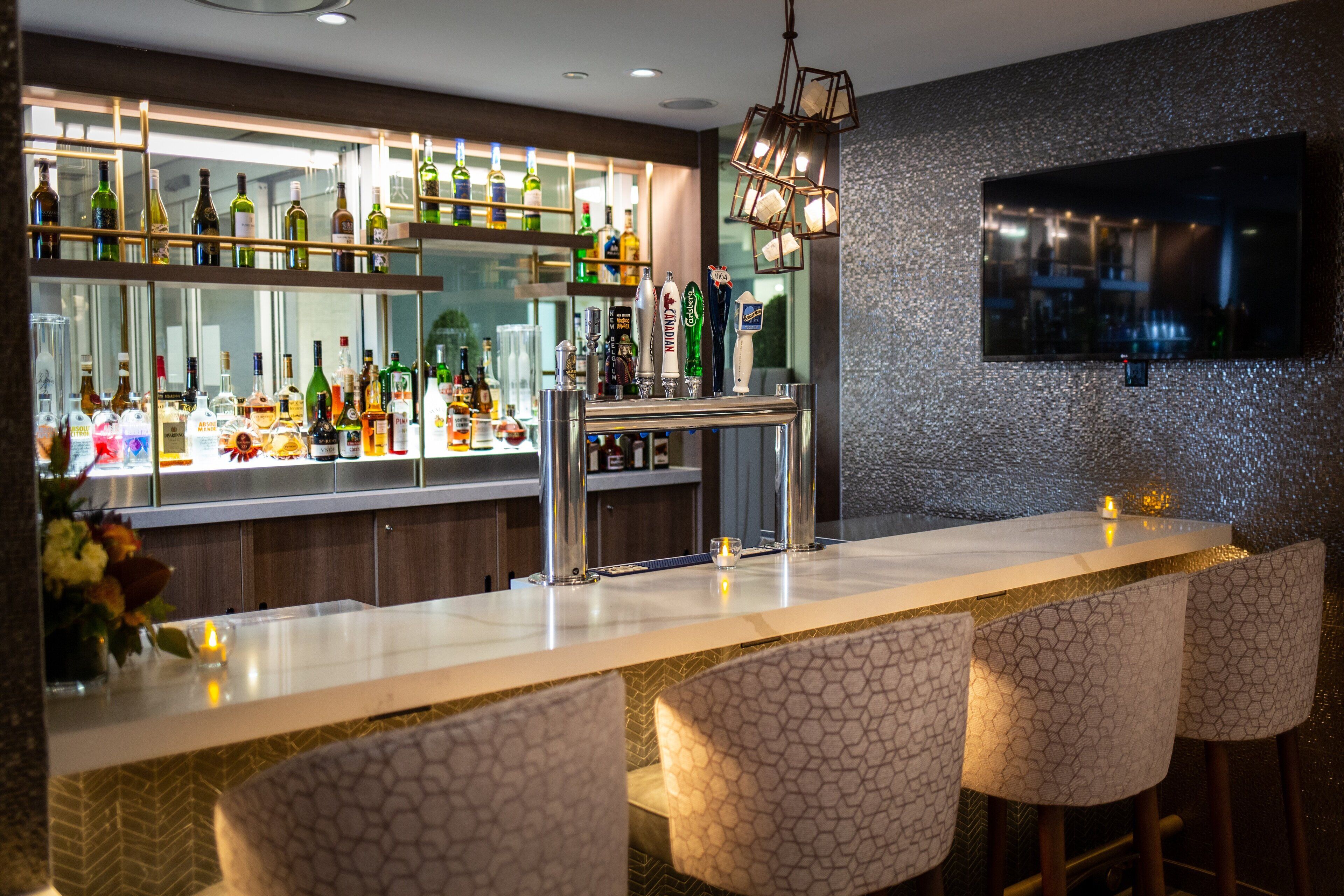 A bar area with a long counter, multiple stools, and a variety of bottles.