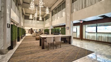 Een ruime lobby met een centraal zitgedeelte, een hoog plafond met hangende lampen en een modern design met marmeren vloeren en groene wanden.