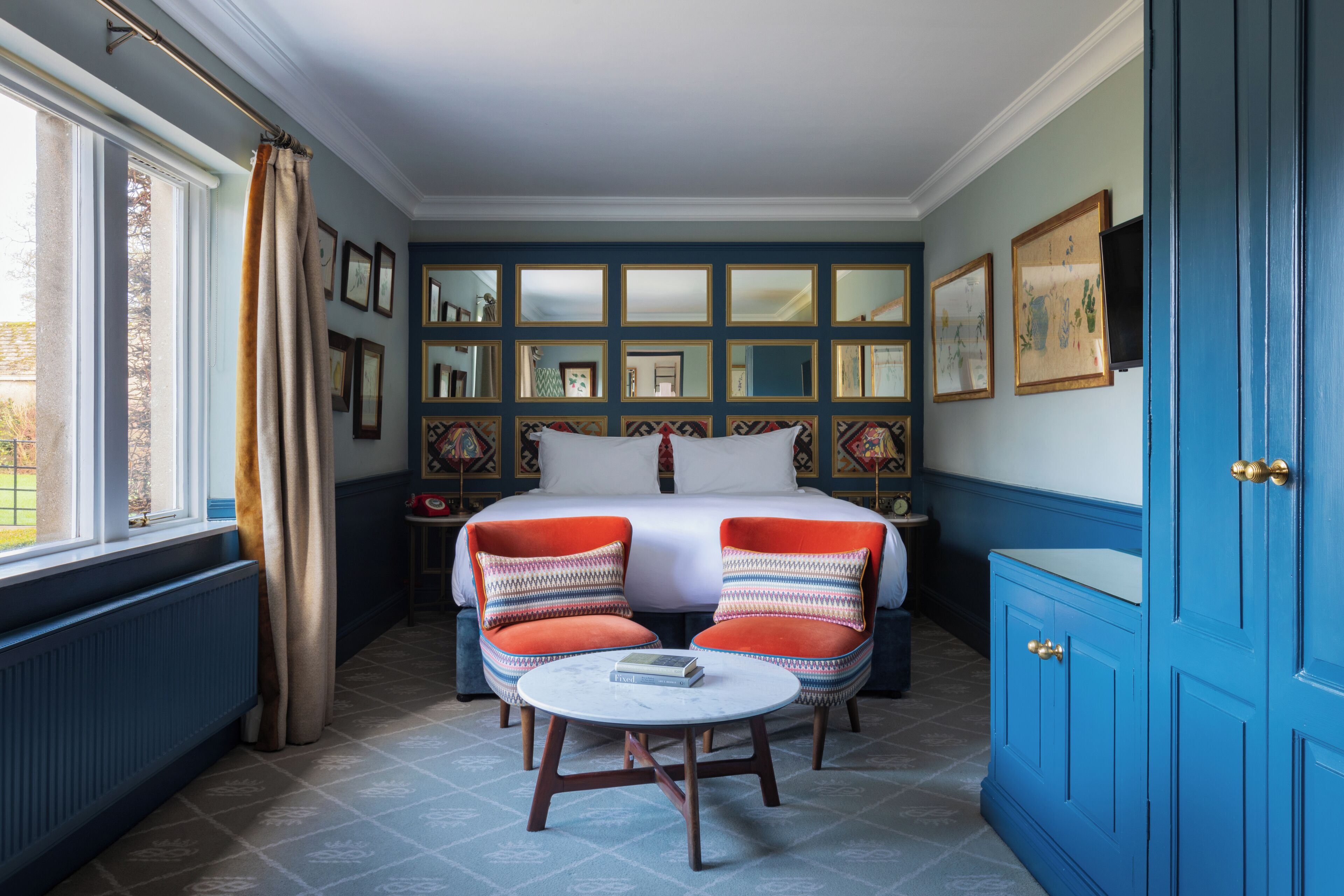 A bedroom with a bed, two chairs, a table, and a blue cabinet.