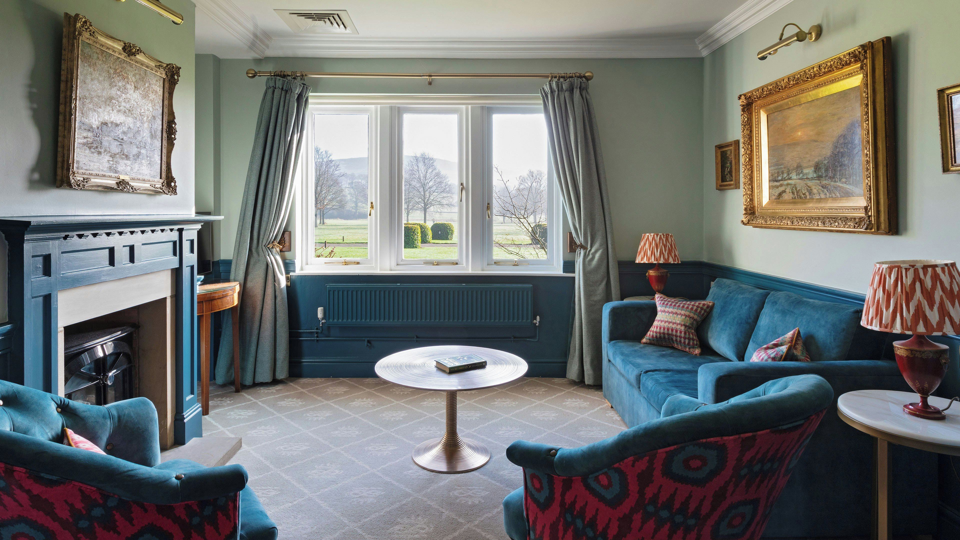A room with a fireplace, a blue sofa, a round table, and a view of the outdoors through a window.