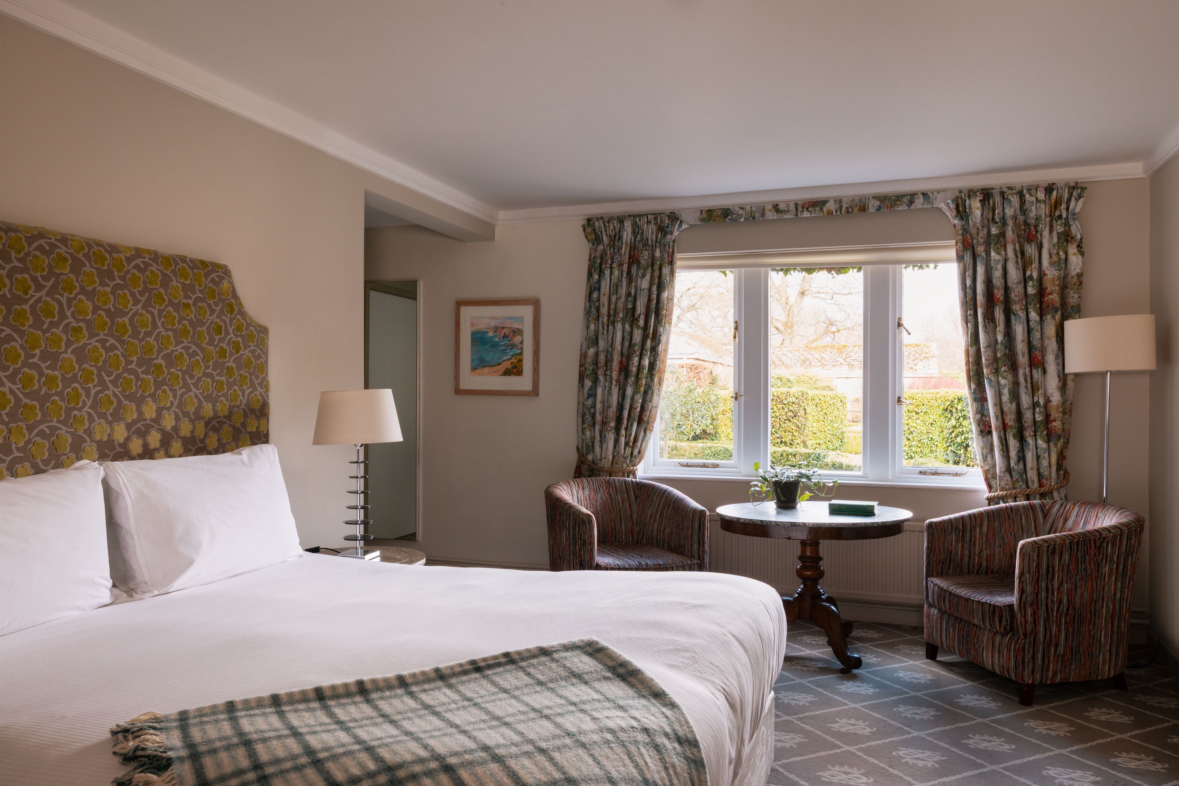 A hotel room with a large bed, two armchairs, a small table, and a window with curtains.