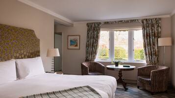 A hotel room with a large bed, two armchairs, a small table, and a window with curtains.