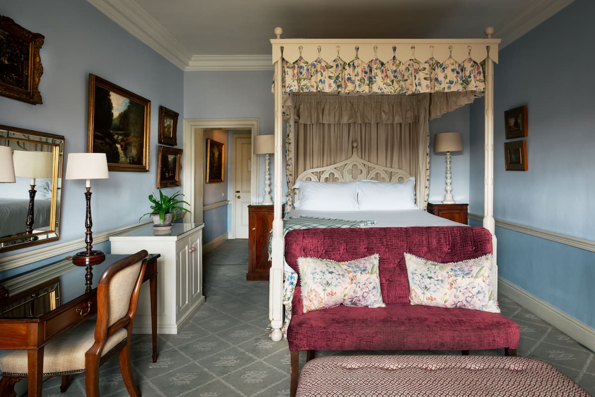 A bedroom with a four-poster bed, a desk with a chair, and a red upholstered bench.