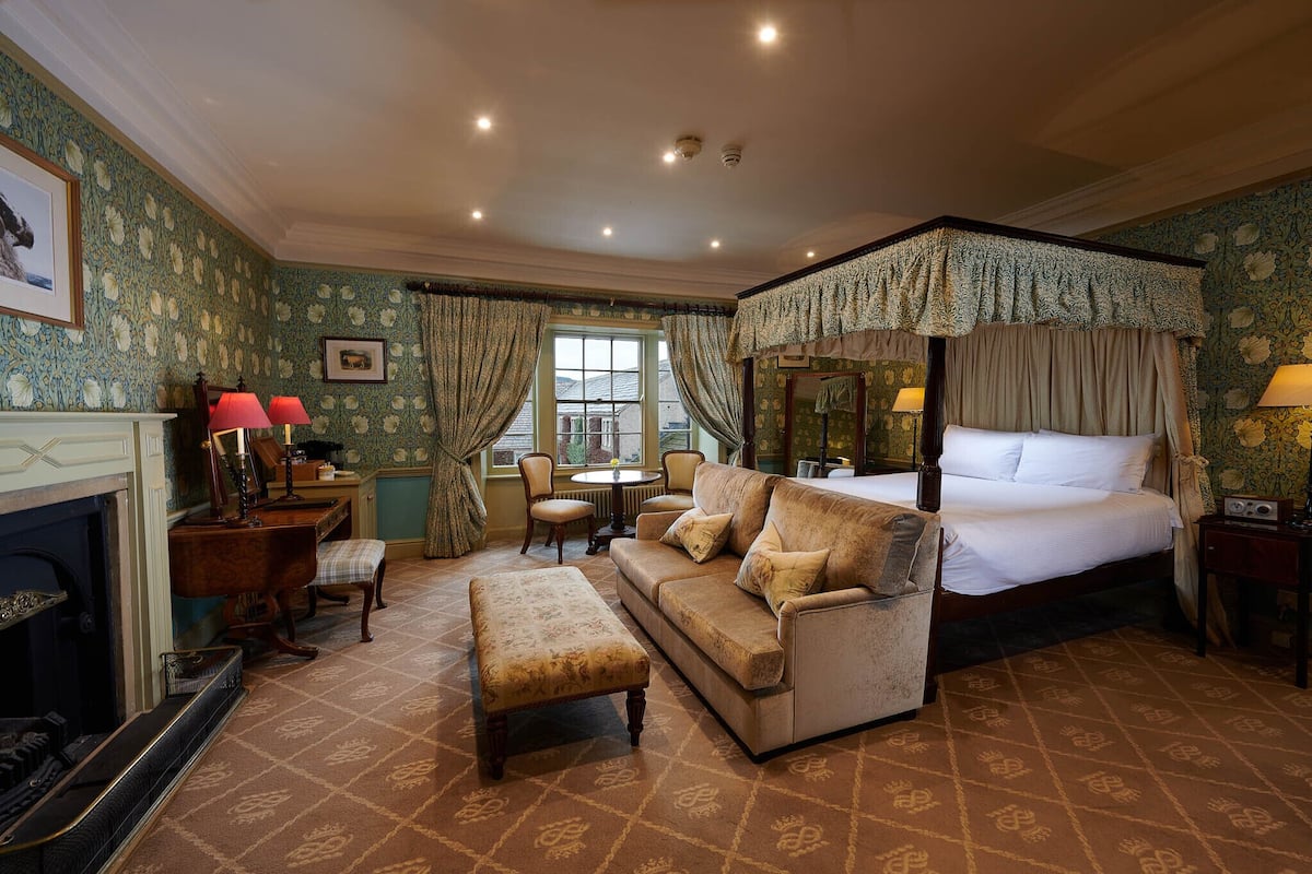 A traditional bedroom with a four-poster bed, a sofa, a fireplace, and a dining table.