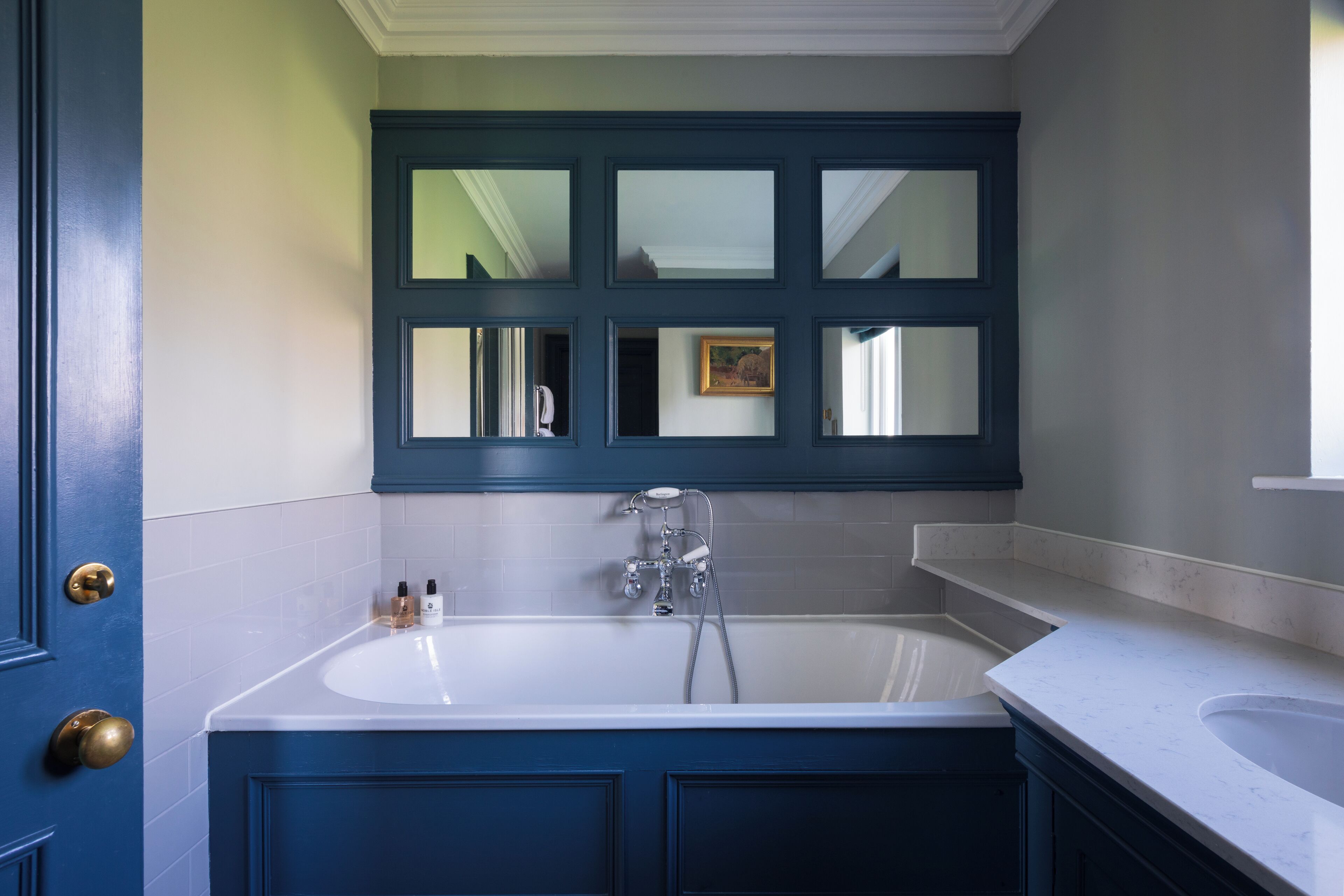 A bathroom with a large bathtub, a mirror above the tub, and a door with a brass handle.