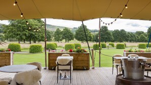 An outdoor seating area with round tables and chairs, a wooden bench with a sign, and a metal pot on a table. - The Devonshire Arms Hotel (Skipton)