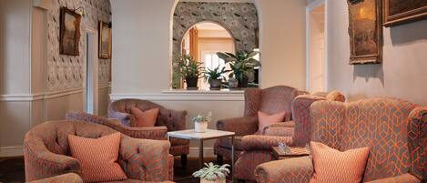 A cozy living room with patterned armchairs, a small table, and potted plants.
