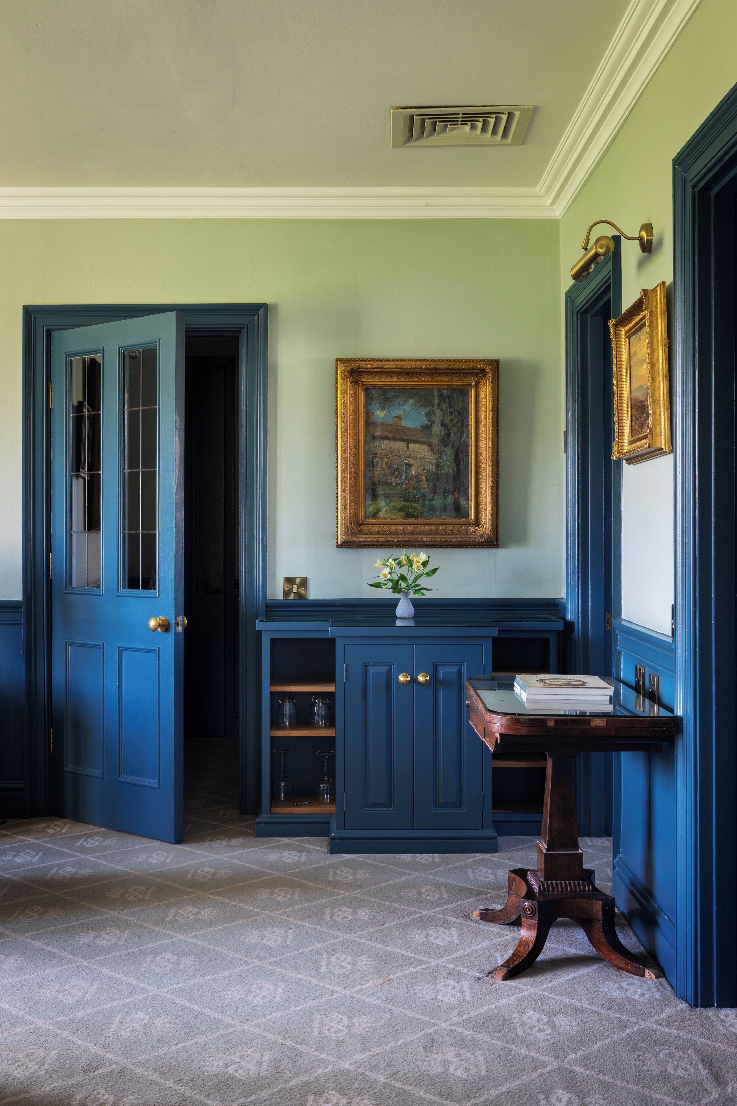 A room with blue walls, a wooden table, a painting, and a door leading to another room.
