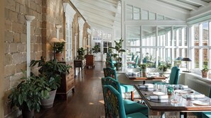 Un amplio comedor con mesas y sillas de madera, plantas en macetas y una pared de ladrillo.