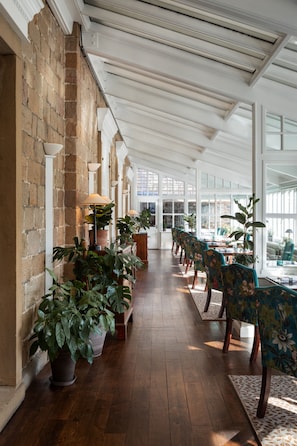 A long corridor with wooden flooring, potted plants, and a series of tables and chairs. - The Devonshire Arms Hotel (Skipton)