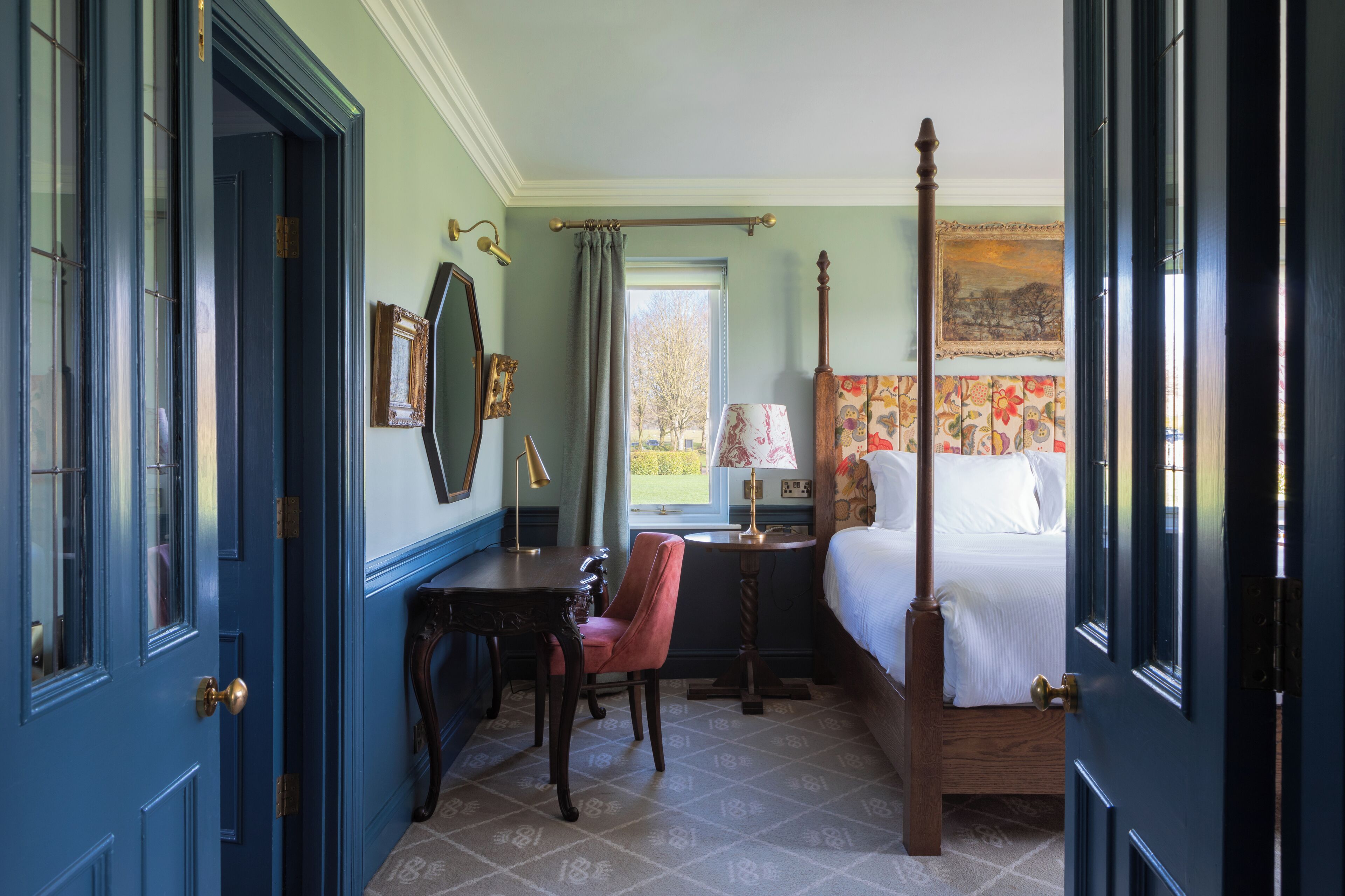 Une chambre à coucher avec un lit à baldaquin, un bureau, une chaise, une table de chevet et une fenêtre donnant sur l’extérieur.