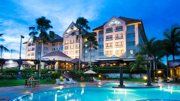 A hotel with a swimming pool, palm trees, and a well-lit facade. - Le Grandeur Balikpapan (Balikpapan)