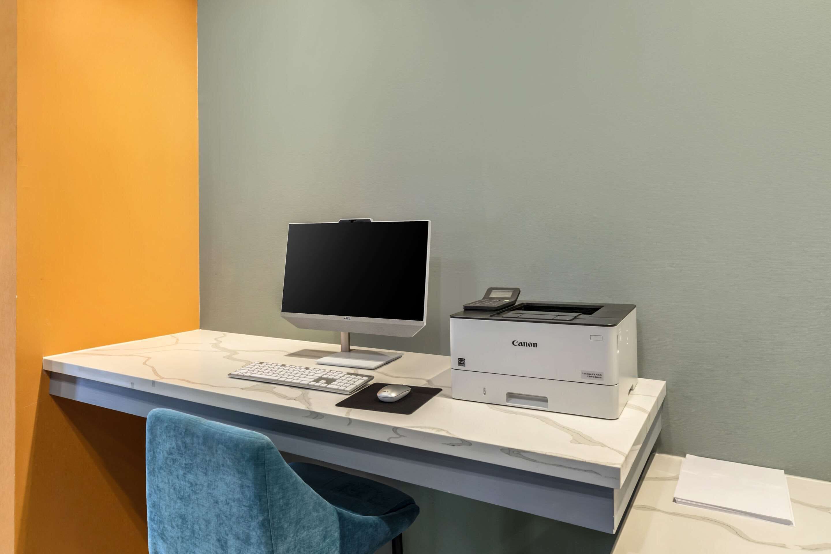 A modern office desk with a desktop computer, a Canon printer, a keyboard, a mouse, and a chair.