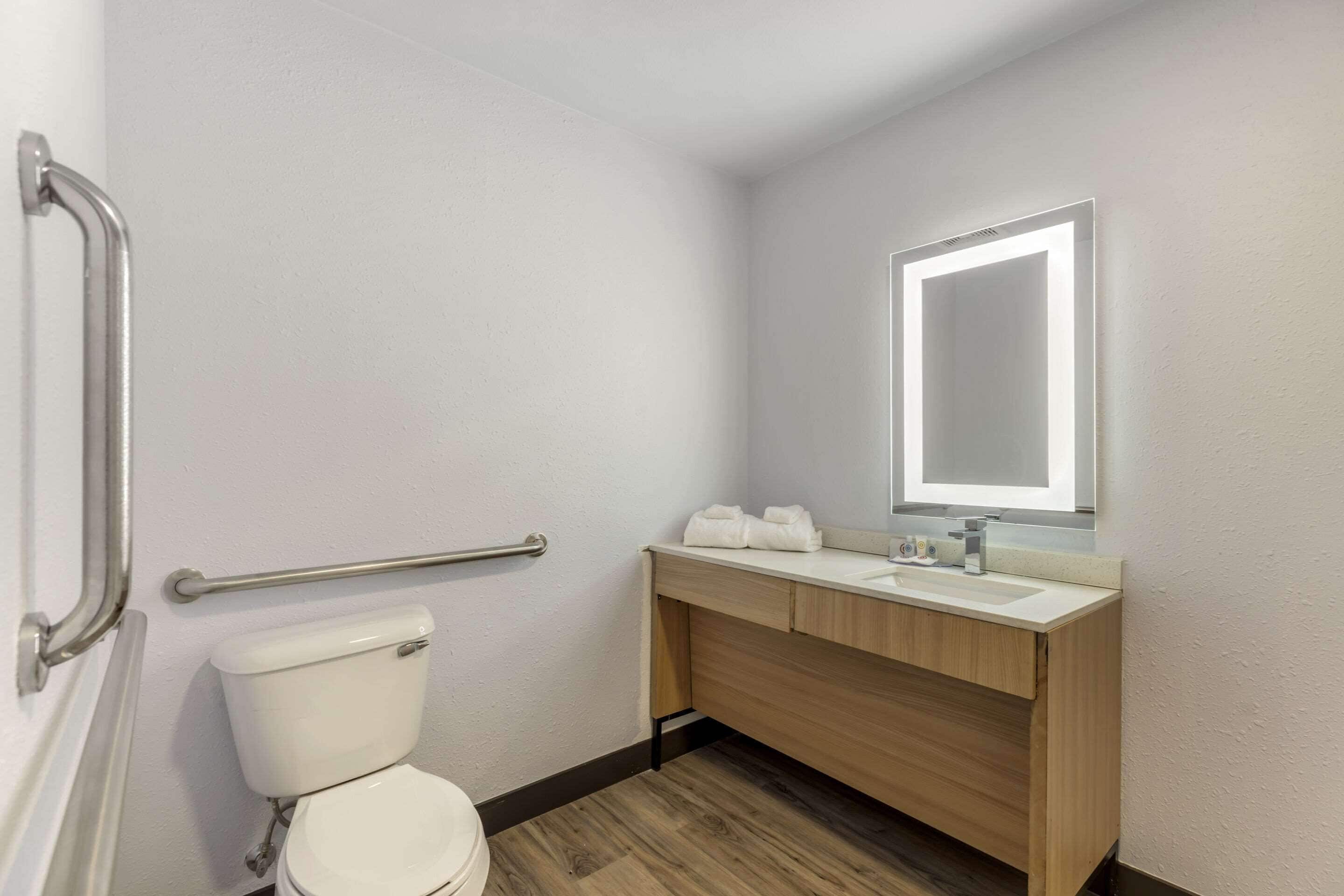 A bathroom with a toilet, a wooden vanity with a mirror, and a handrail.