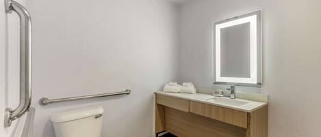 A bathroom with a toilet, a wooden vanity with a mirror, and a handrail.