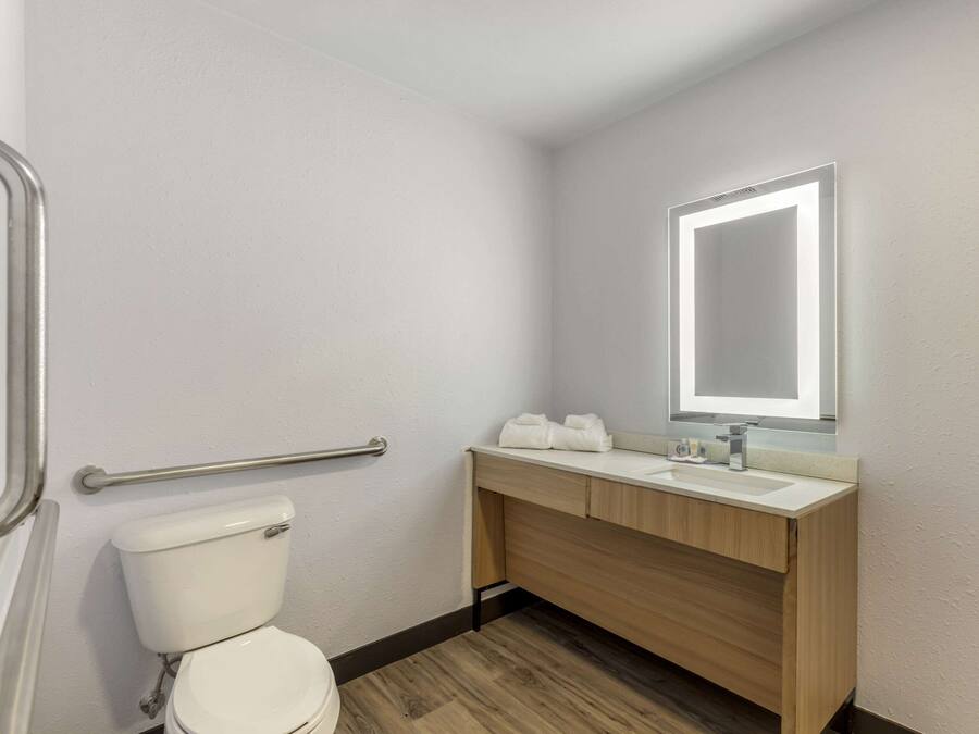 A bathroom with a toilet, a wooden vanity with a mirror, and a handrail.