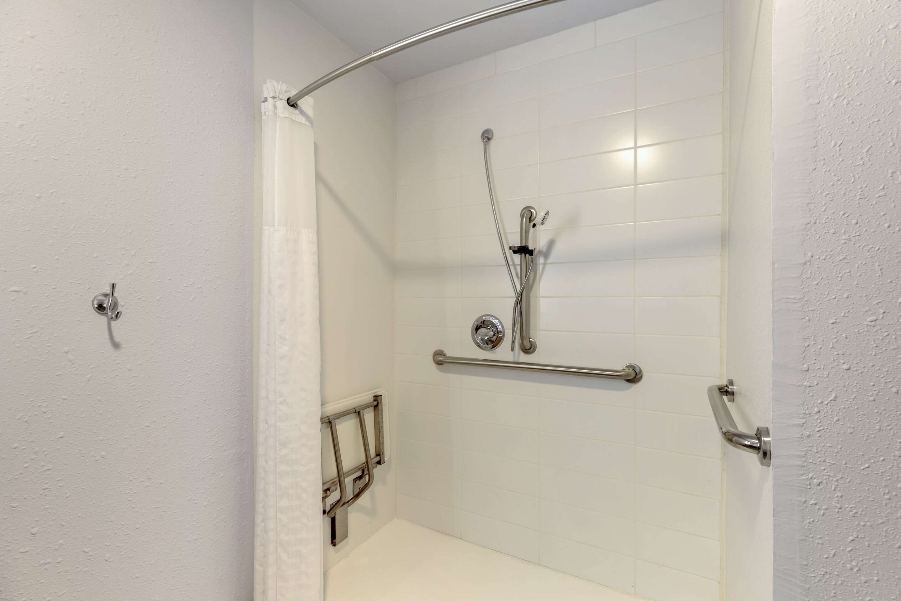 A shower with a grab bar, a showerhead, and a white tiled wall.