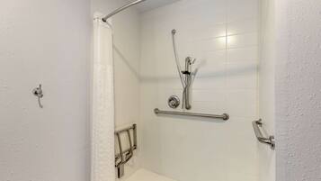 A shower with a grab bar, a showerhead, and a white tiled wall.