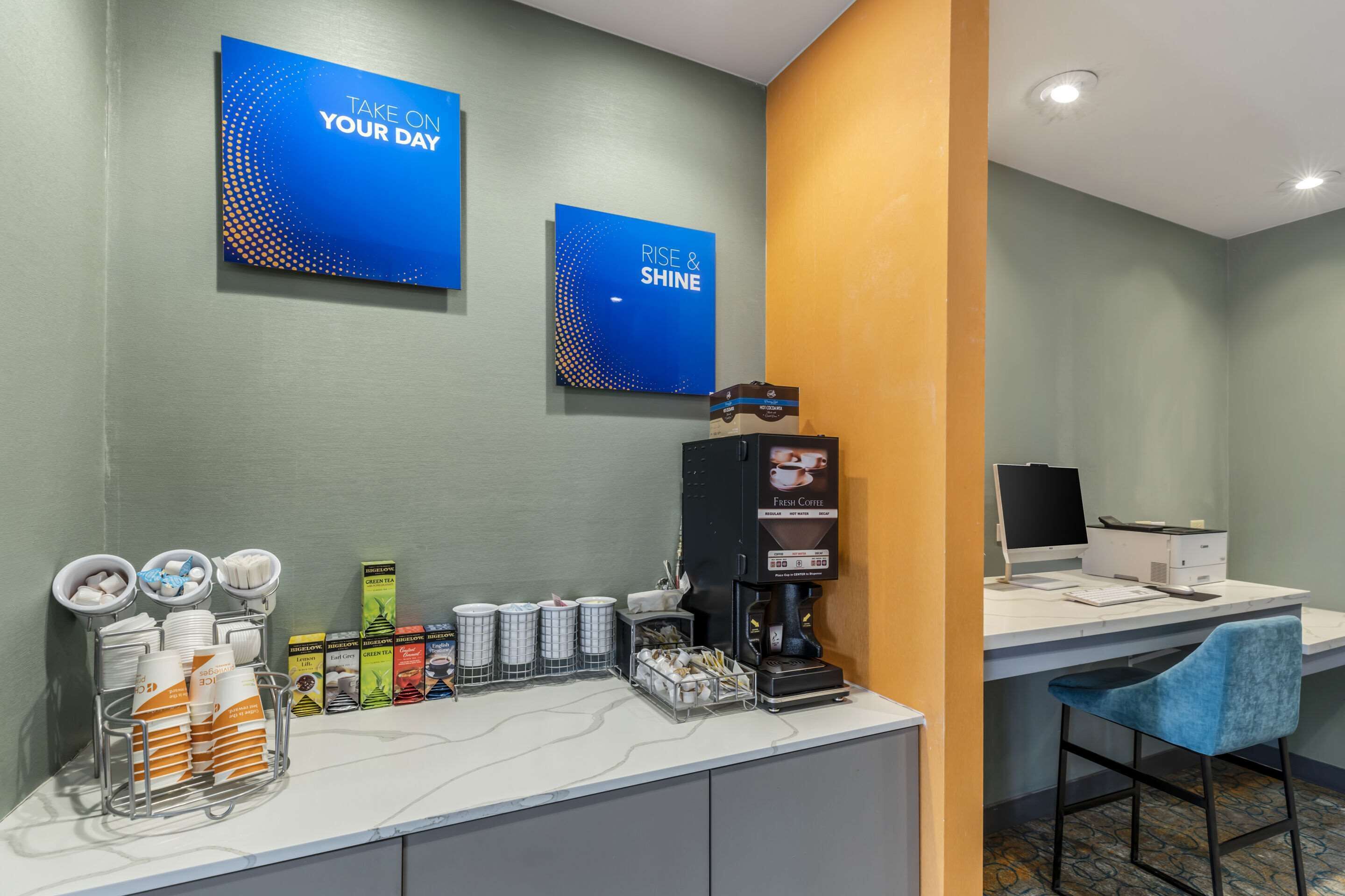 A hotel reception area with a coffee station, a computer, and a seating area.