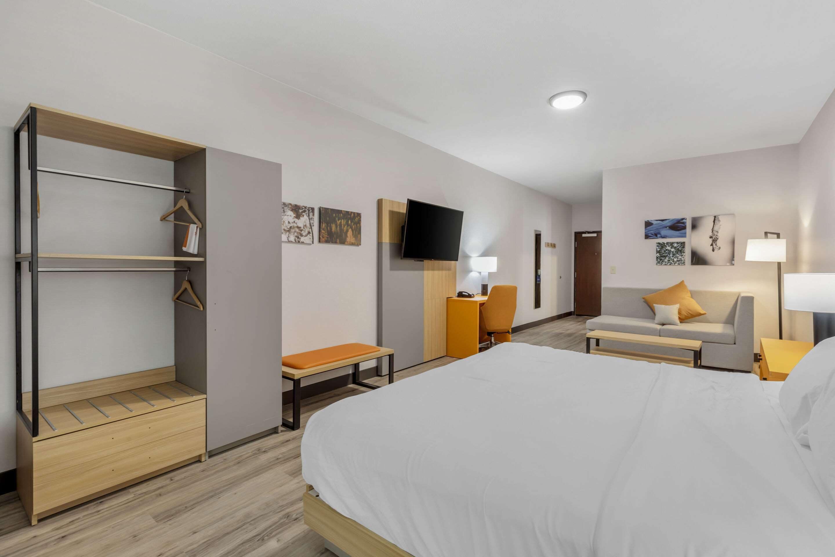 Habitación de hotel con cama, escritorio, silla, sofá, televisión y armario.