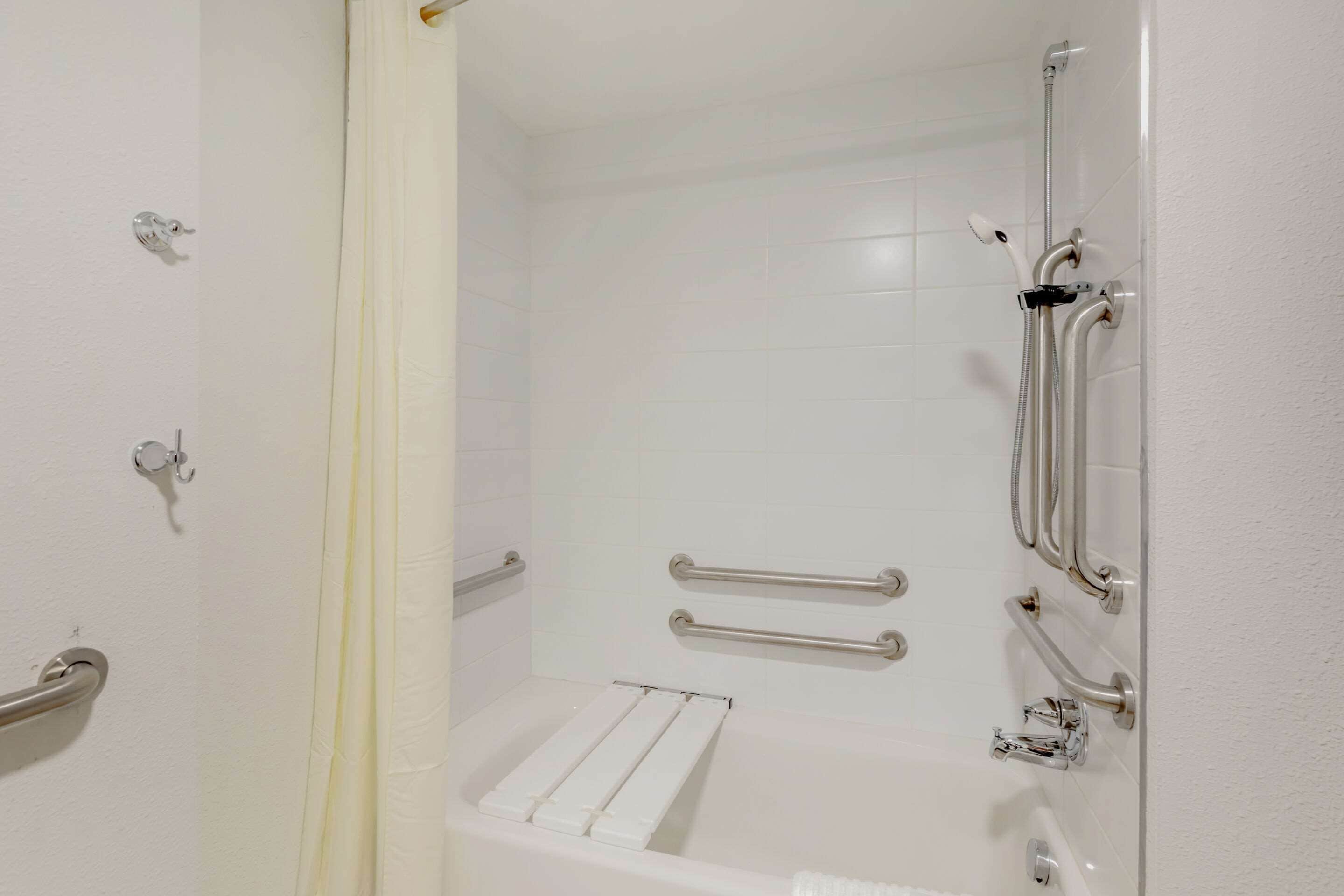 Une salle de bain blanche avec une douche, des barres d’appui et une baignoire blanche.