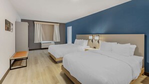 A hotel room with two beds, a small table, a chair, and a window with curtains.
