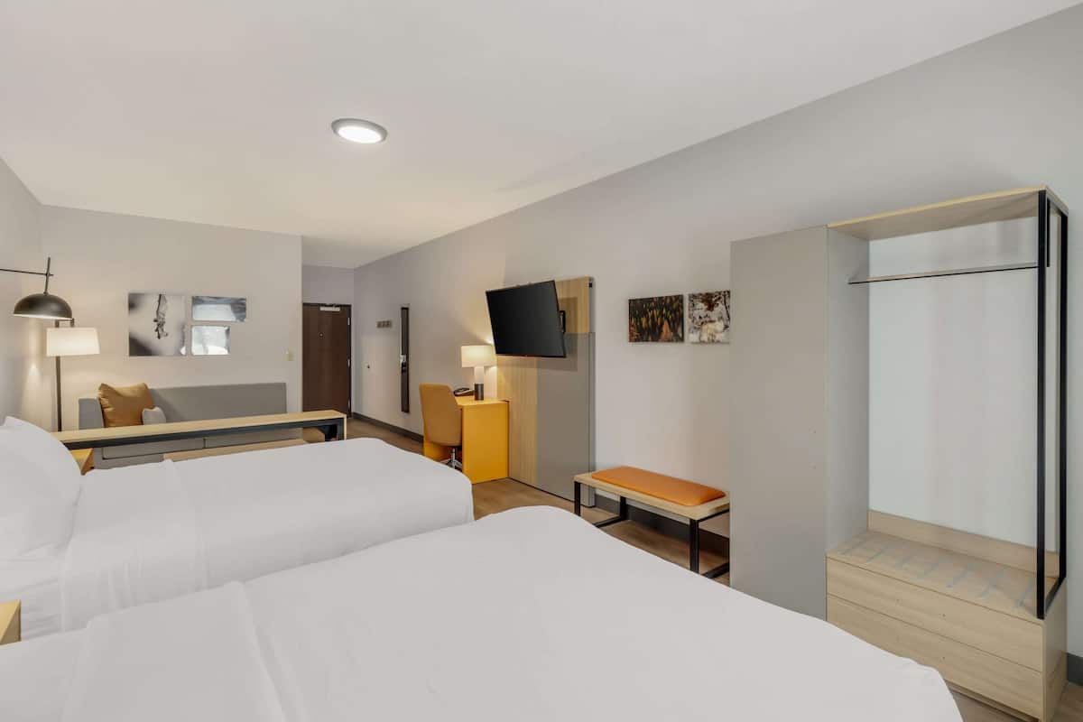 Une chambre d’hôtel avec deux lits, un bureau, une chaise, une télévision et une armoire.
