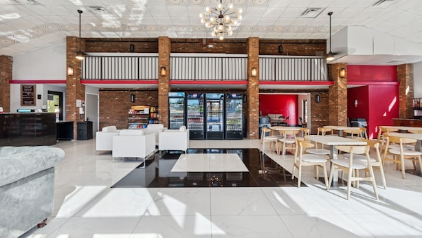 A spacious lobby with a high ceiling, a central black reflective floor, and a seating area with white and wooden furniture. - Ramada by Wyndham Temple Terrace/Tampa North (Tampa)