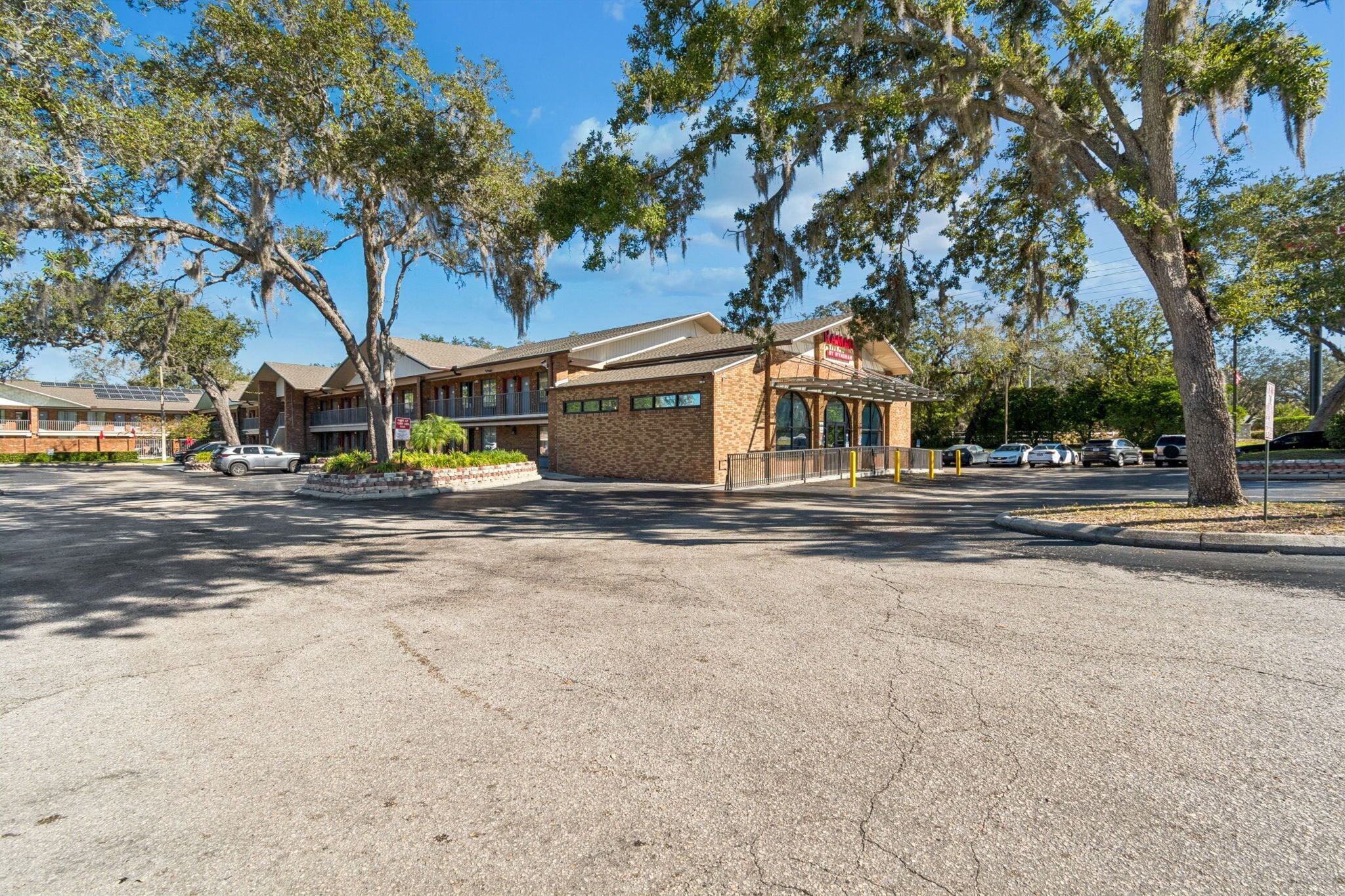 A motel with a brick facade, a covered parking area, and trees with Spanish moss.
