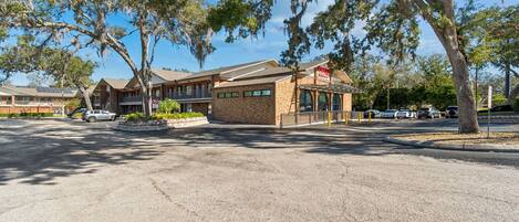 A motel with a brick facade, a covered parking area, and trees with Spanish moss.